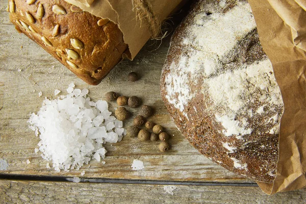 Δύο καρβέλια ψωμί συσκευασμένα σε χαρτί σε ξύλινο τραπέζι με αλάτι και σκεύος. Καλλιεργημένη φωτογραφία. — Φωτογραφία Αρχείου