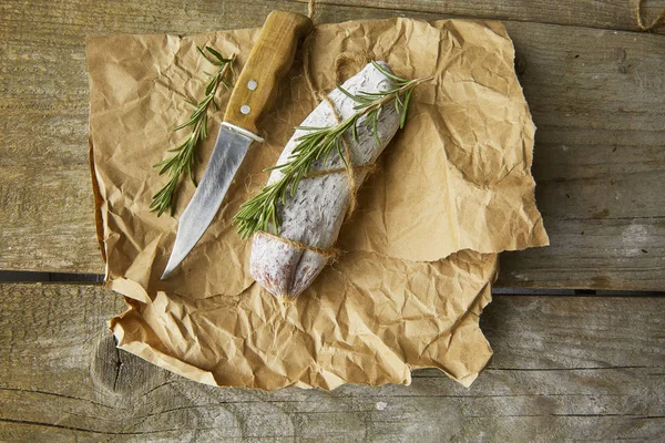 全体イタリアのサラミ wih ローズマリー、紙の上のナイフです。素朴なスタイル。トップ ビュー. — ストック写真