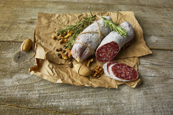Italian salami wih sea salt, rosemary, garlic and nuts on paper. Rustic style. Top view.