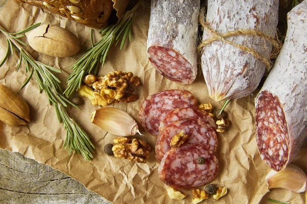 Italienische Salami mit Meersalz, Rosmarin, Knoblauch und Nüssen auf Papier. Rustikaler Stil. Nahaufnahme. — Stockfoto