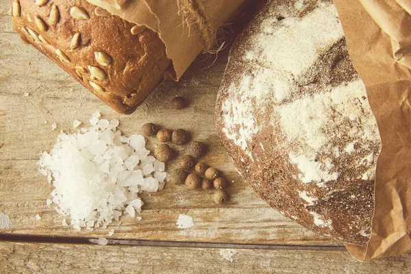 Two Loaves of Bread packed in paper on wooden table with salt and papper. Cropped photo.