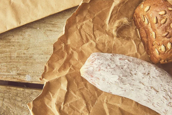 Whole Italian salami wih bread on paper. Rustic style. Cropped photo. — Stock Photo, Image