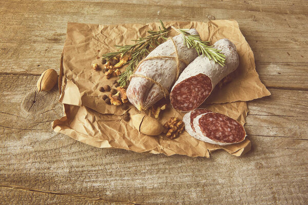 Italian salami wih sea salt, rosemary, garlic and nuts on paper. Rustic style. Top view.