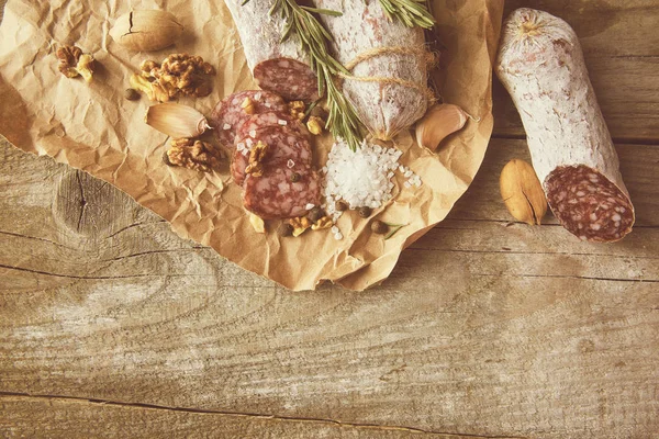 Ιταλικό σαλάμι με θαλασσινό αλάτι, δενδρολίβανο, σκόρδο και ξηρούς καρπούς σε χαρτί. Ρουστίκ στυλ. Άνω όψη. — Φωτογραφία Αρχείου