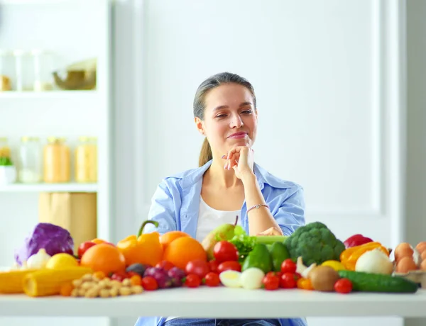 Jeune et mignonne femme assise à la table pleine de fruits et légumes à l'intérieur en bois. — Photo