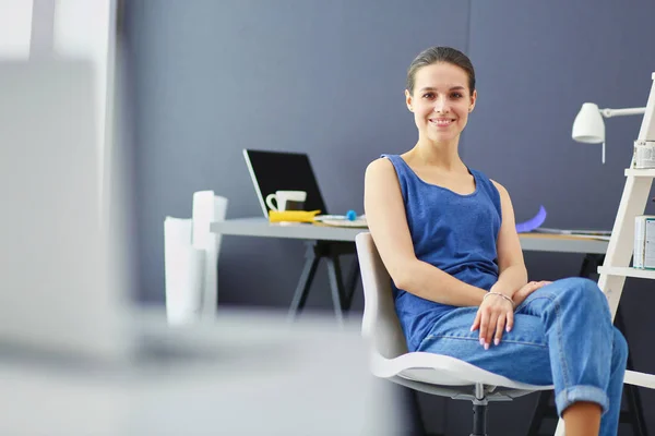 Jonge vrouw zit aan het bureau met instrumenten, plan en laptop. — Stockfoto