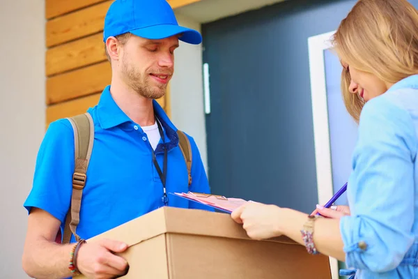 Repartidor sonriente con uniforme azul que entrega la caja de paquetes al destinatario: concepto de servicio de mensajería. Repartidor sonriente en uniforme azul — Foto de Stock