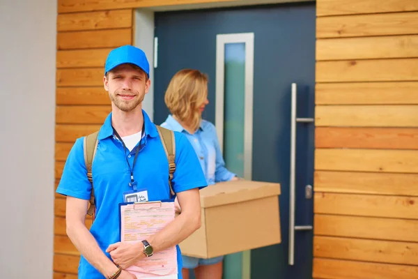 Repartidor sonriente con uniforme azul que entrega la caja de paquetes al destinatario: concepto de servicio de mensajería. Repartidor sonriente en uniforme azul — Foto de Stock