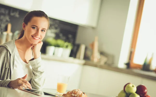 Mujer joven con jugo de naranja y tableta en la cocina —  Fotos de Stock