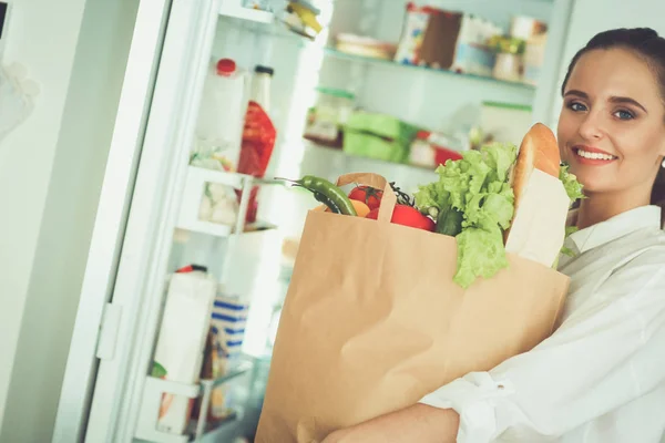 Giovane donna che tiene borsa della spesa con verdure. In piedi in cucina — Foto Stock