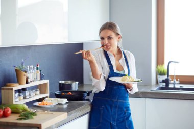 Mutfakta sobanın yanında duran genç bir kadın.