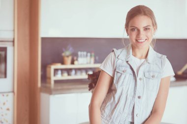 Kollarını mutfak arka planında kavuşturmuş genç bir kadının portresi.