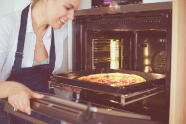 Mutlu genç bayan evde pizza pişiriyor.