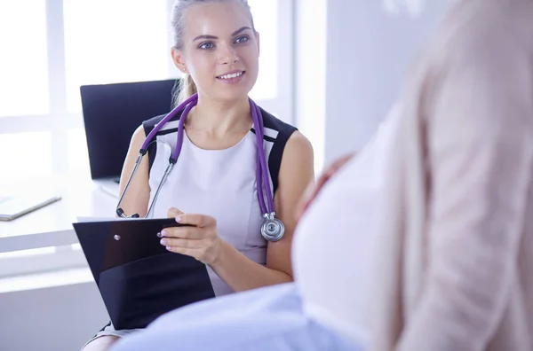 Jovem médica com estetoscópio e tablet falando com mulher grávida no hospital. — Fotografia de Stock