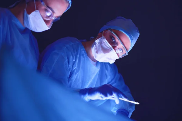 Ärzteteam in der Chirurgie vor dunklem Hintergrund. — Stockfoto