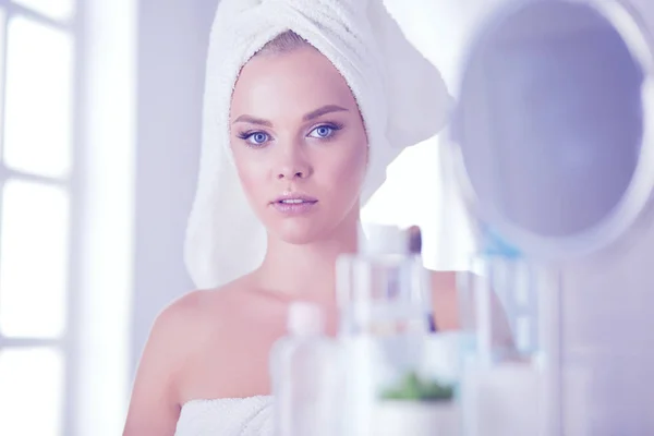 Mujer joven en albornoz mirando en el espejo del baño —  Fotos de Stock