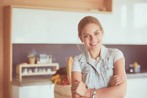 Mujer joven sosteniendo bolsa de la compra de comestibles con verduras. De pie en la cocina —  Fotos de Stock