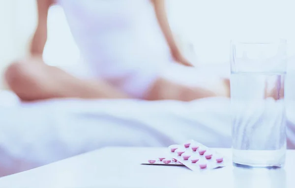 Young beautiful woman with pills lying on bed in bedroom — Stock Photo, Image