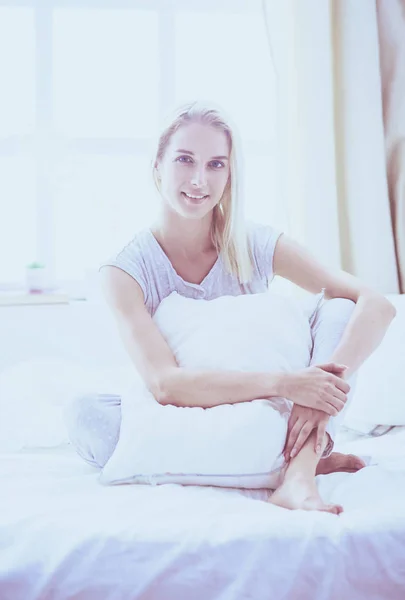 Mujer linda sosteniendo una almohada mientras está sentada en su cama — Foto de Stock