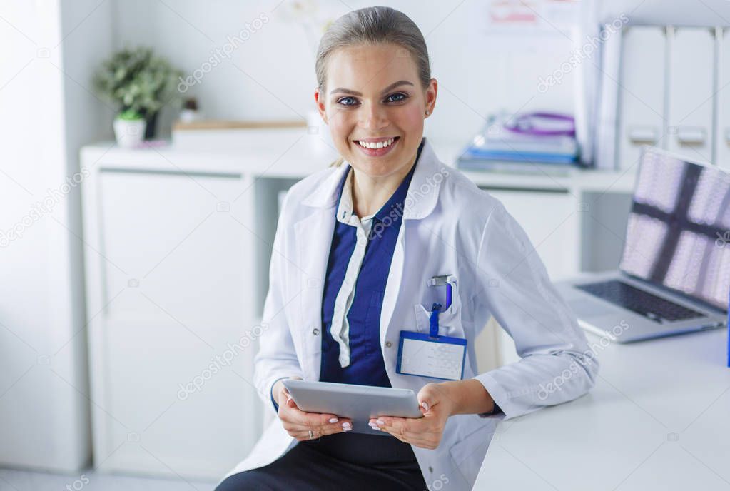 Portrait of woman doctor at hospital corridor, holding tablet computer, looking at camera, smiling
