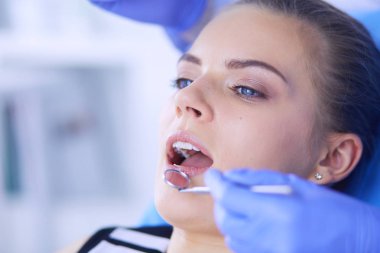 Dişçi muayenehanesinde diş muayenesi yapan ağzı açık genç bir kadın hasta..