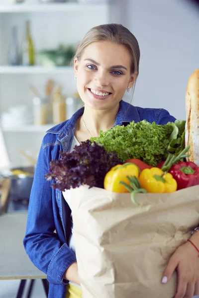 Jovem mulher segurando supermercado saco de compras com legumes .Standing na cozinha — Fotografia de Stock