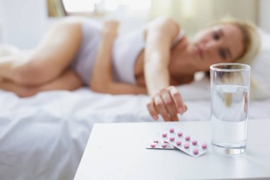 Genç, güzel bir kadın. Yatağında haplarla yatıyor.