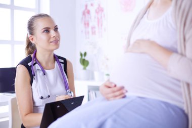 Steteskoplu ve tabletli genç kadın doktor hastanede hamile bir kadınla konuşuyor..