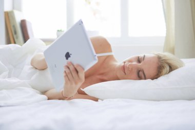 Elinde boş ekranlı dijital tablet tutan ve yatak odasında kameraya gülümseyen bir kız.