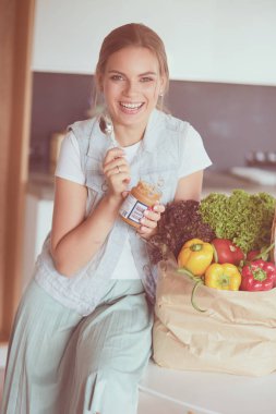 Sebzeli alışveriş poşeti taşıyan genç bir kadın. Mutfakta duruyor.