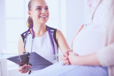 Steteskoplu ve tabletli genç kadın doktor hastanede hamile bir kadınla konuşuyor..