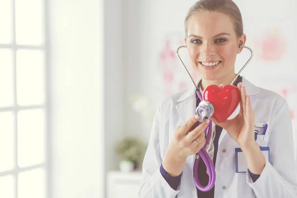 Un médico con estetoscopio examinando el corazón rojo, aislado sobre fondo blanco — Foto de Stock