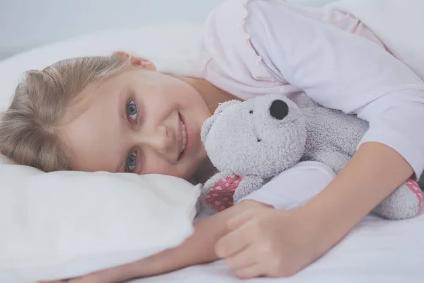 Barn lilla flicka sover i sängen med en leksak nallebjörn. — Stockfoto
