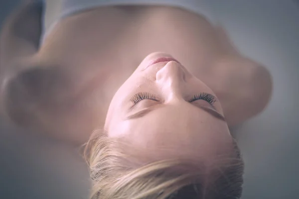 Mujer joven acostada en una mesa de masaje, relajándose con los ojos cerrados. Una mujer. Salón de spa — Foto de Stock