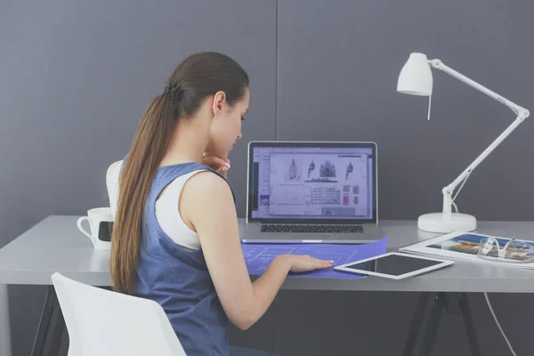 Jovem sentada na mesa com instrumentos, plano e laptop. — Fotografia de Stock