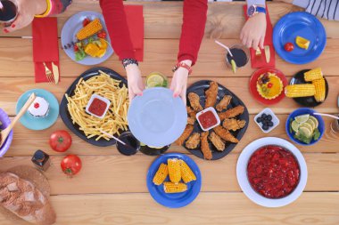 Ahşap masada otururken birlikte yemek yiyen bir grup insanın üst düzey görüntüsü. Masada yemek var. İnsanlar fast food yiyor..