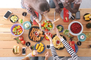 Ahşap masada otururken birlikte yemek yiyen bir grup insanın üst düzey görüntüsü. Masada yemek var. İnsanlar fast food yiyor..