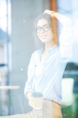 Ofis masasında dizüstü bilgisayarıyla oturan genç bir kadın. Pencereden bakıyor. Genç kadın.
