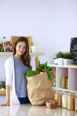 Bakkal alışveriş çantası sebzeli tutan genç kadın. Mutfakta ayakta. Genç kadın