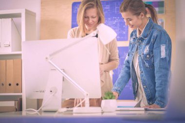 Masanın yanında duran iki genç kadın enstrüman, plan ve dizüstü bilgisayarla.