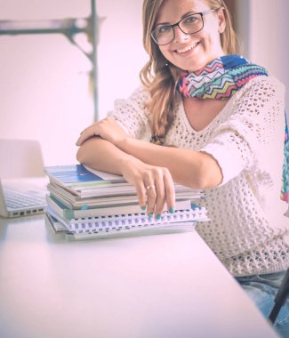 Kitapların arasında bir masada oturan genç bir kadın. Öğrenci