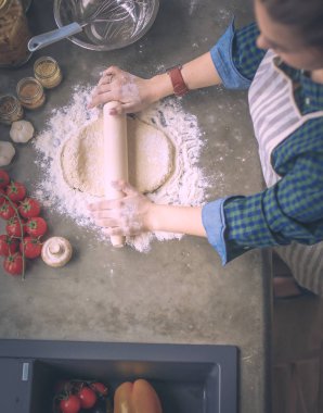 Güzel bir kadın mutfakta pasta pişiriyor. Masanın yanında duruyor..