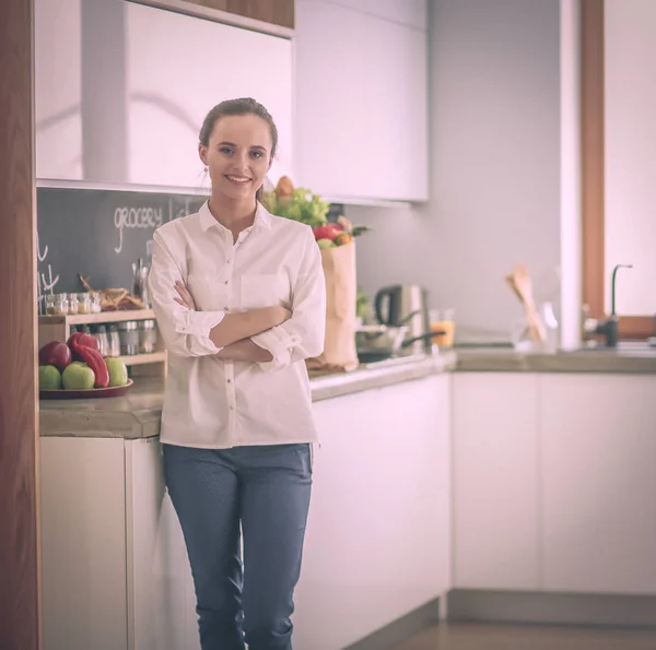 Portrét mladé ženy stojící s rukama zkříženýma proti pozadí kuchyně. Žena v kuchyni. — Stock fotografie