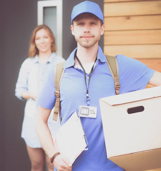 Repartidor sonriente con uniforme azul que entrega la caja de paquetes al destinatario: concepto de servicio de mensajería. Repartidor sonriente en uniforme azul — Foto de Stock