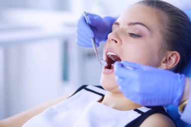 Dişçi muayenehanesinde diş muayenesi yapan ağzı açık genç bir kadın hasta..