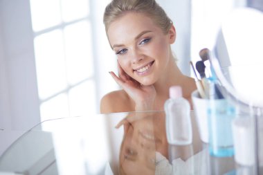 Bornozlu genç kadın banyo aynasına bakıyor..