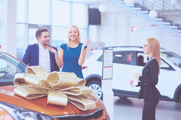 Een man maakt een geschenk - een auto aan zijn vrouw. Ze is hier verbaasd over. Ze zijn hier erg blij mee. — Stockfoto