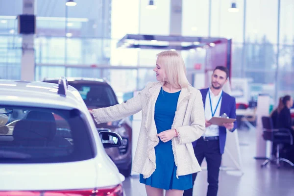 Negociante com mulher fica perto de um carro novo no showroom — Fotografia de Stock