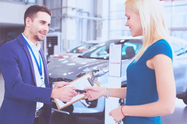 Prodavač aut prodává auto šťastnému zákazníkovi v prodejně aut a předává klíče — Stock fotografie