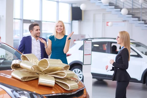 Een man maakt een geschenk - een auto aan zijn vrouw. Ze is hier verbaasd over. Ze zijn hier erg blij mee. — Stockfoto